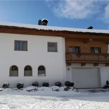 Ein gemütliches Haus im Alpenstil mit einem überdachten Balkon. Die Umgebung ist schneebedeckt und der Himmel ist teilweise bewölkt.