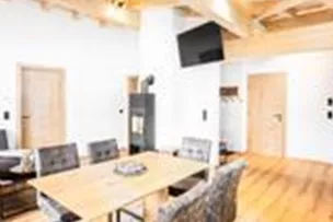 Das Appartement Villaggio bietet ein modernes Wohn-Esszimmer mit Holzdecken, großen Fenstern und einen Kaminofen. Es gibt einen Esstisch aus Holz, gemütliche Sitzmöbel und Zugang zu einem großen Balkon. Am Balkon befindet sich ein Tisch mit Stühlen, welche zum Verweilen einladen. Genießen Sie den Blick auf den Wilden Kaiser und das Dorf Going am Wilden Kaiser.