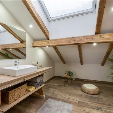 A modern bathroom with wooden ceilings and large windows. There is a sink on a wooden shelf and decorative plants.
