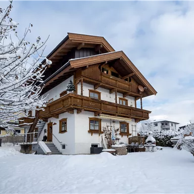 A cozy house in traditional style, surrounded by snow-covered trees. The sky is cloudy and conveys a wintry atmosphere.