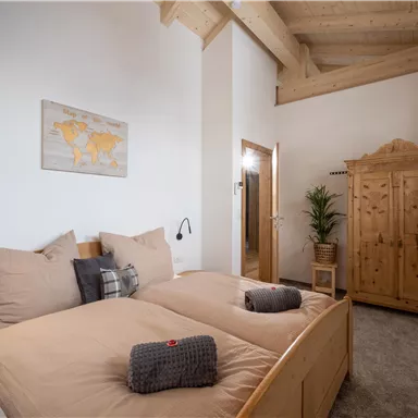 A modern bedroom with a double bed, cozy pillows, and a wooden wardrobe. A world map hangs on the wall, and a plant creates a pleasant atmosphere.