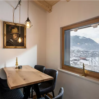 A cozy room with a wooden table and modern chairs. The window offers a view of a snowy landscape.