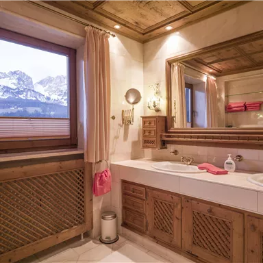 Ein stilvolles Badezimmer mit Holzverkleidung und einer Badewanne. Durch das Fenster ist ein Blick auf schneebedeckte Berge zu sehen.