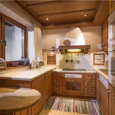 Eine moderne Küche aus Holz mit hellen Wänden und großen Fenstern. Die Ausstattung umfasst einen Herd, eine Spüle und eine gemütliche Ecke mit einem kleinen Tisch.