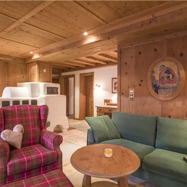 Ein gemütlicher Wohnraum mit Holzdecke und rustikalen Möbeln. Eine rote Sessel mit kariertem Muster und eine grüne Couch laden zum Entspannen ein.