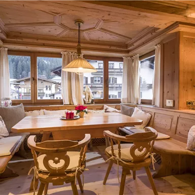 Ein gemütlicher Essbereich aus Holz mit einem großen Tisch und bequemen Sitzplätzen. Durch die Fenster sieht man eine winterliche Landschaft.