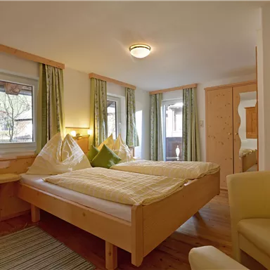 A cozy room with two beds and wood-paneled walls. Bright curtains and an armchair create an inviting atmosphere.