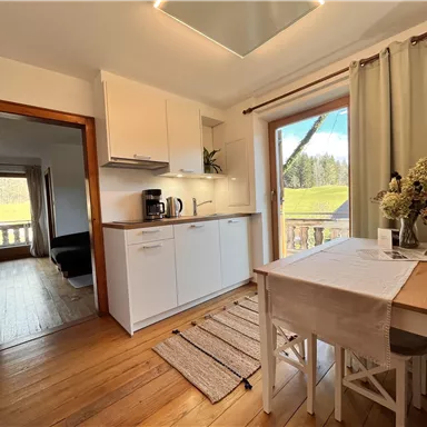 Eine helle, moderne Küche mit einem Esstisch und Blick auf die Natur. Eine gemütliche Atmosphäre mit Holzfußboden und frischen Blumen.