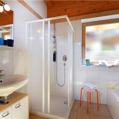 A modern bathroom with a shower cabin and a sink. A window provides daylight and there are some towels on a shelf.