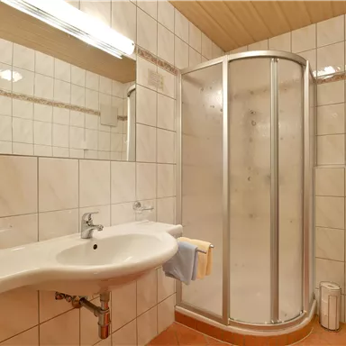 Ein modernes Badezimmer mit Duschkabine und einem Waschbecken. Die Wände sind gefliest und der Raum ist hell und sauber.