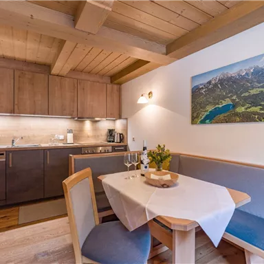 Eine moderne Küchenecke mit Holzdetails und einem Essbereich. An der Wand hängt ein Bild von einer Berglandschaft.