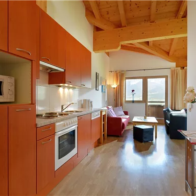 A modern kitchenette with wooden cabinets and home electronics. The living area is bright and cozy, with a sofa and windows that let in natural light.