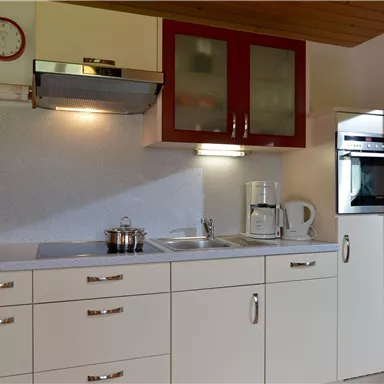 Eine moderne Küche mit weißen Schränken und roten Akzenten. Sie verfügt über einen Herd, einen Kühlschrank und eine Kaffeemaschine.