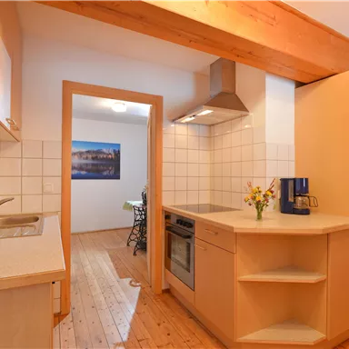 A modern kitchen with wooden shelves and an open space. The walls are brightly tiled, and there is a small flower decoration on the countertop.