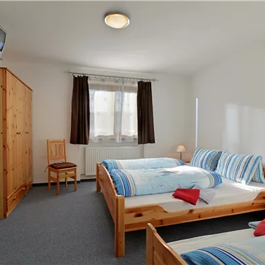 Ein helles Zimmer mit zwei Betten und einer gemütlichen Atmosphäre. Es gibt einen Tisch, einen Stuhl und einen kleinen Schrank.