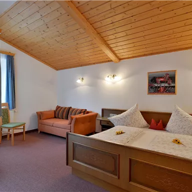 Ein gemütliches Hotelzimmer mit Holzdecke und zwei betten. Es gibt ein Sofa und ein Fenster mit Vorhang.