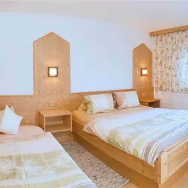 Ein gemütliches Zimmer mit zwei Betten aus Holz und hellen, sanften Farben. Große Fenster sorgen für viel Tageslicht und eine einladende Atmosphäre.