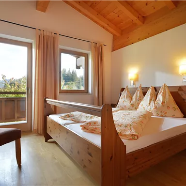 A cozy bedroom with a double bed and wooden furniture. Large windows let in plenty of daylight and offer a nice view outside.