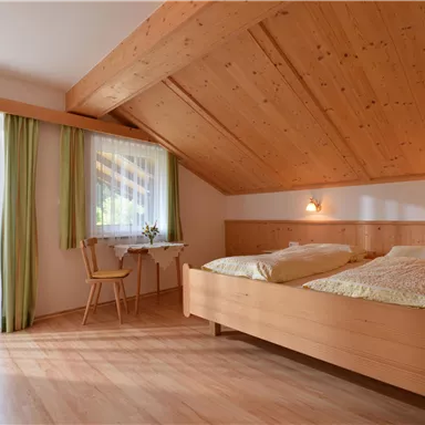 A cozy bedroom with wooden walls and two single beds. Large windows with curtains allow plenty of light in.