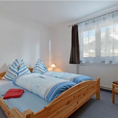 Ein gemütliches Schlafzimmer mit einem Doppelbett und zwei Nachttischen. Das Zimmer hat helle Wände und ein Fenster mit Vorhängen.