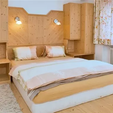 Ein gemütliches Schlafzimmer mit einem großen Bett und Holzmöbeln. Der Raum hat helle Vorhänge und eine warme, einladende Atmosphäre.