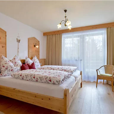 A cozy bedroom with two beds and wood-paneled walls. Large windows allow plenty of daylight and create an inviting atmosphere.