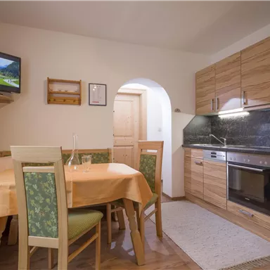 Eine gemütliche Küchenzeile mit Holzschränken und modernen Geräten. Ein runder Tisch mit Stühlen sowie eine kleine Essecke sorgen für eine einladende Atmosphäre.