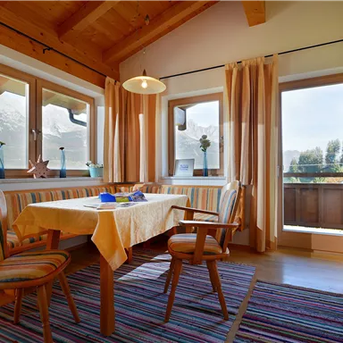 A cozy dining area with a wooden table and chairs. Large windows provide a view of the mountains and plenty of daylight.