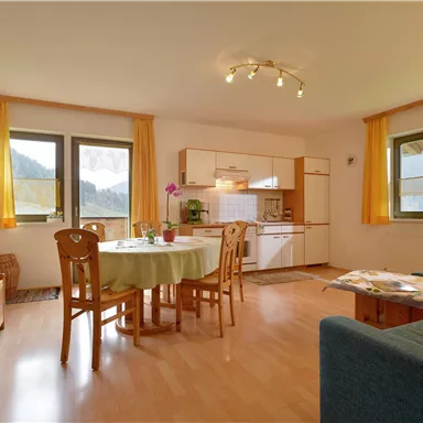 Eine helle und gemütliche Wohnküche mit einem Esstisch und Stühlen. Große Fenster bieten einen Blick auf die Natur.