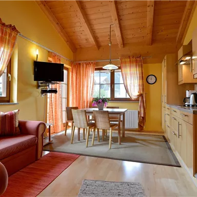 Eine gemütliche Küche mit einem Essbereich und einem roten Sofa. Die Wände sind gelb gestrichen und große Fenster bieten viel Tageslicht.