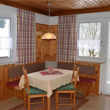 Ein gemütlicher Essbereich mit Holzvertäfelung und großen Fenstern. Der Tisch ist eingedeckt und es gibt bequeme Sitzgelegenheiten.