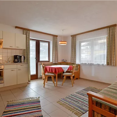 Eine gemütliche, moderne Küche mit einem Essbereich und einem Sofa. Große Fenster sorgen für viel Licht im Raum.