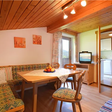 Ein gemütlicher Wohnbereich mit einer Sitzecke und einem Esstisch. Die Wände sind in warmen Farben gehalten und eine Tür führt in eine kleine Küche.