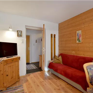 Ein gemütlicher Wohnraum mit einem roten Sofa und einem Fernseher. Die Wände sind teilweise aus Holz, was eine warme Atmosphäre schafft.