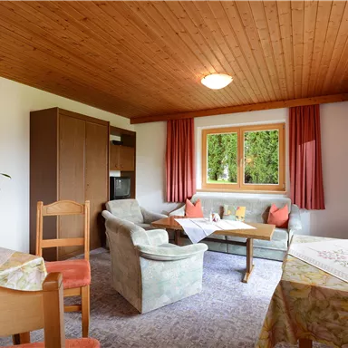 Ein gemütlicher Wohnbereich mit einem Essplatz und einem Sofa. Große Fenster lassen viel Licht herein und bieten einen Blick ins Grüne.