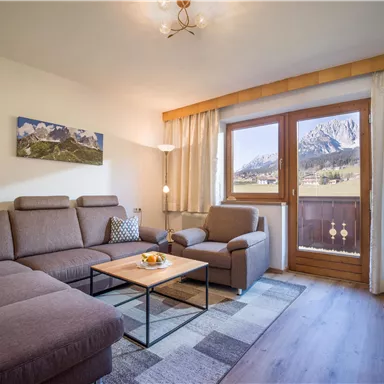 Ein gemütliches Wohnzimmer mit einem modernen Sofa und einem Sessel. Große Fenster bieten einen Blick auf die Berge und viel natürliches Licht.