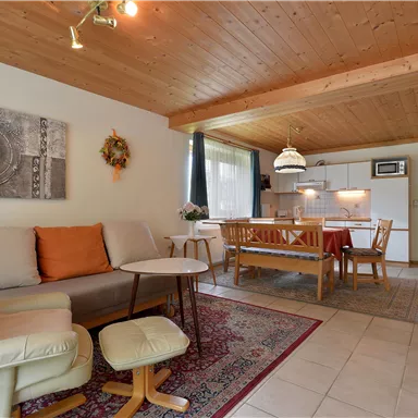 Ein gemütliches Wohnzimmer mit Holzdecke, einem bequemen Sessel und einem Essbereich. Die Raumgestaltung ist hell und einladend.