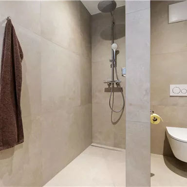 A modern shower with gray tiles and a showerhead. Two brown towels hang on the wall.