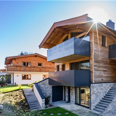 A modern house with wood and stone cladding. In the background, more traditional buildings can be seen.