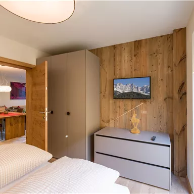A modern bedroom with a bed, a wardrobe, and a decorative TV on the wall. The wood paneling gives the room a warm atmosphere.