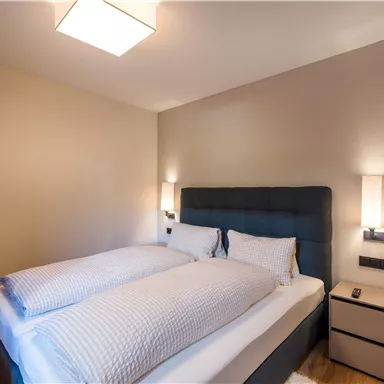 A modern bedroom with a double bed and soft colors. The walls are light, and there is pleasant lighting.