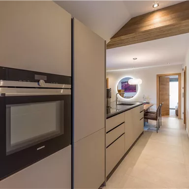 A modern kitchen with elegant furniture and a bright space. The refrigerator and the oven are built-in, and there is a dining area with chairs.