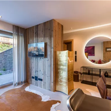 A modern living room with wooden walls and large windows. The room is stylishly furnished with a table, a mirror, and a TV.