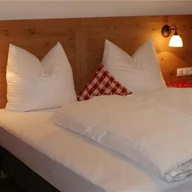 Ein gemütliches Schlafzimmer mit einem Doppelbett und kissenförmigen Kopfkissen. Die Wände sind mit Holz verkleidet und die Vorhänge sind rotkariert.