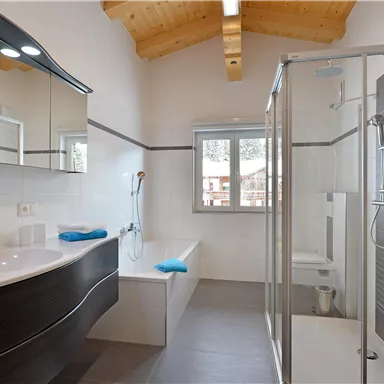 Ein modernes Badezimmer mit hellem Holzdecke und eleganten Sanitäranlagen. Es gibt eine Dusche, eine Badewanne und stilvolle Waschbecken mit blauen Handtüchern.