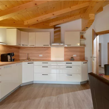 Eine moderne Küche mit hellen Schränken und einer Holzdecke. Der Raum ist großzügig und gut ausgestattet.