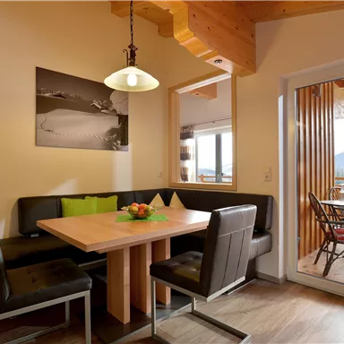 Ein gemütlicher Essbereich mit Holztisch und schwarzen Stühlen. Große Fenster bieten Ausblick auf die Berge und sorgen für viel Tageslicht.