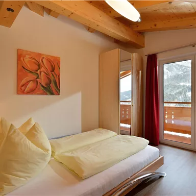 Ein helles Schlafzimmer mit zwei großen Fenstern und einem Balkon. Die Einrichtung ist modern mit Holzdetails und einer gemütlichen Atmosphäre.