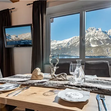 Ein gemütlicher Esstisch mit Blick auf schneebedeckte Berge. Der Raum hat große Fenster, die viel Tageslicht hereinlassen.