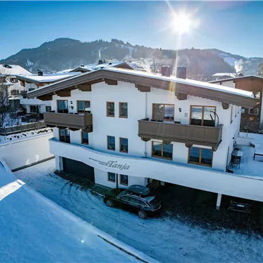 A modern house in the snow with balconies and large windows. The sun is shining over the nearby mountains.